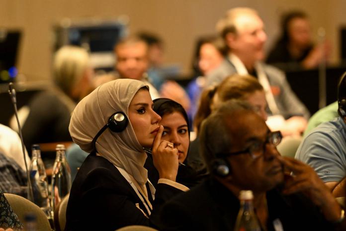 A woman holds a finger up to her mouth as she listens among a large audience at the IPC Membership Gathering.