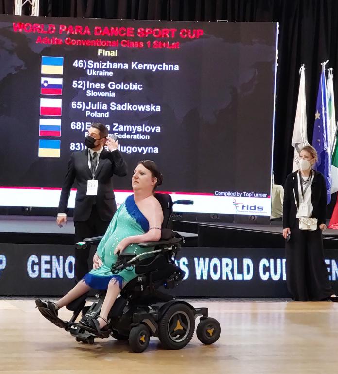 A female dancer in a green dress moves the joystick of her electric wheelchair as she performs in competition.
