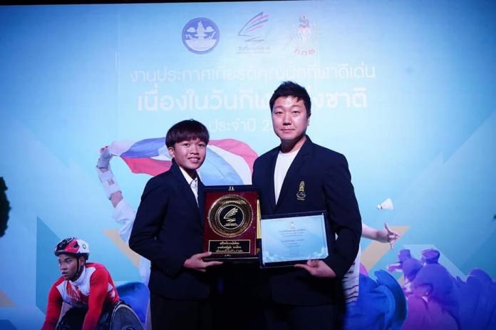 A female athlete and her male coach pose with an honorary plaque and certificate.