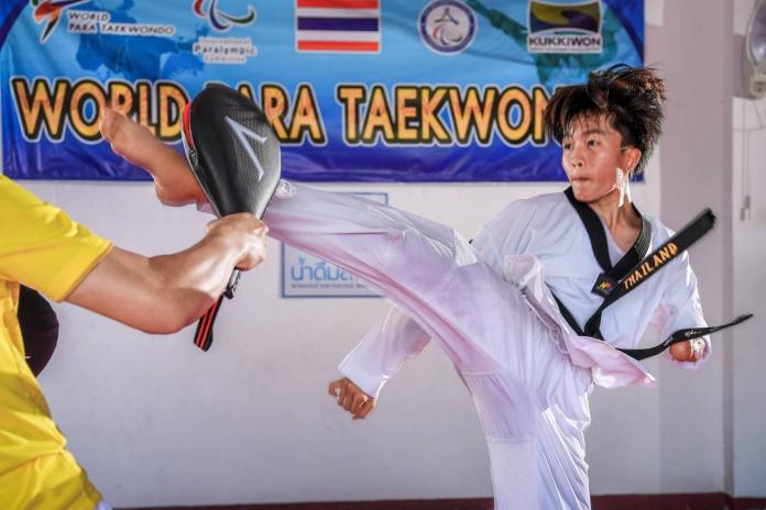 A female Para taekwondo athlete hits a cushion with her right leg during training.