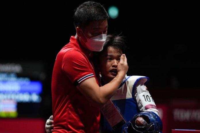 A male coach hugs a female Para taekwondo athlete on the field of play.