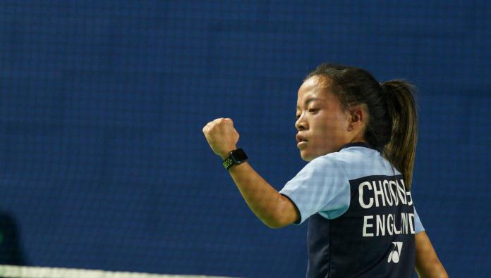 A female athlete pumps her fist in front of a badminton net.