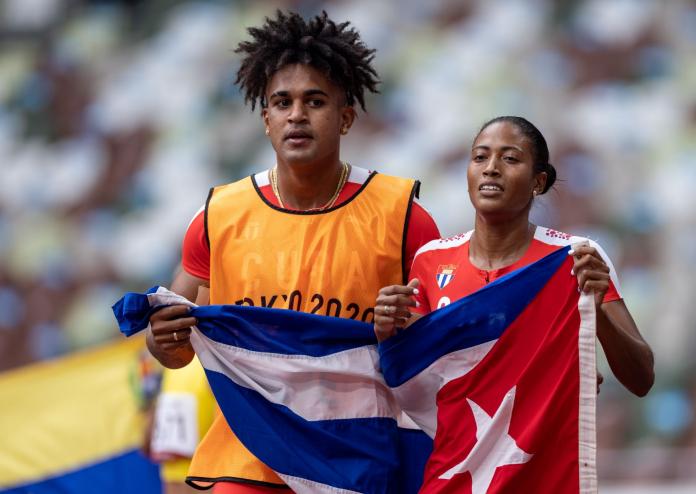 A female Para athlete hold the Cuban flag with her male guide runner
