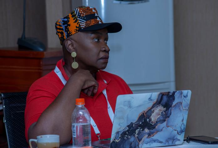 A woman looks on while seated at a table with a laptop in front of her.