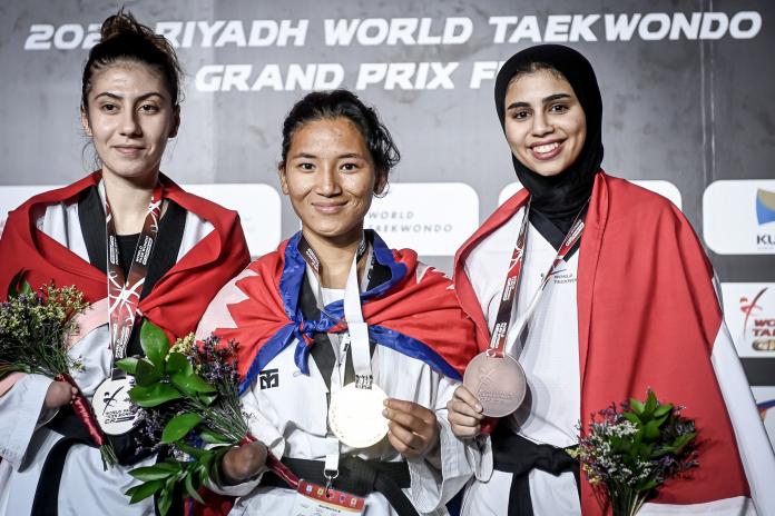Three female athletes smile as they hold their medals on the podium.