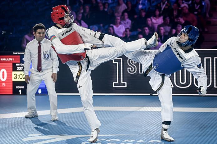 Two male Para taekwondo athletes kick each other during competition.