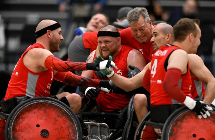 Wheelchair rugby players and staff dressed in red jerseys hug and shake hands at the 2022 Wheelchair Rugby World Championships
