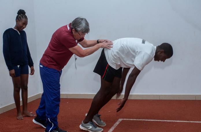 A female coach supports a male athlete as he leans forward at the starting line on a training track.