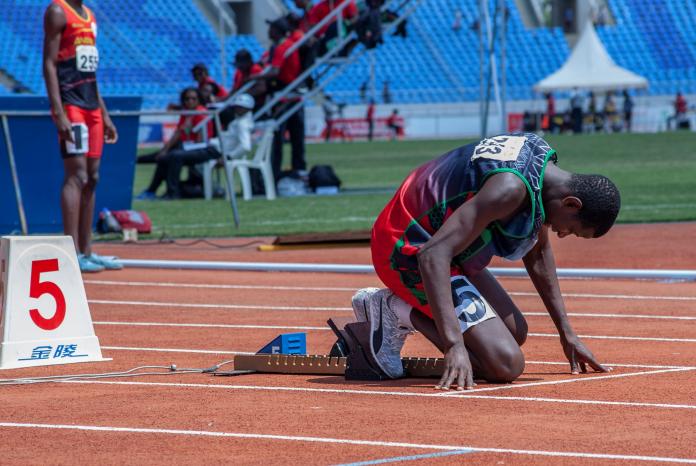 A male sprinter kneels into the starting position at the starting blocks during a competition.