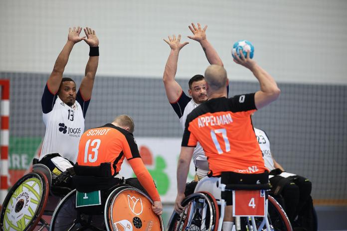 A Dutch player raises his hand holding the ball while two Portuguese players try to block the throw.