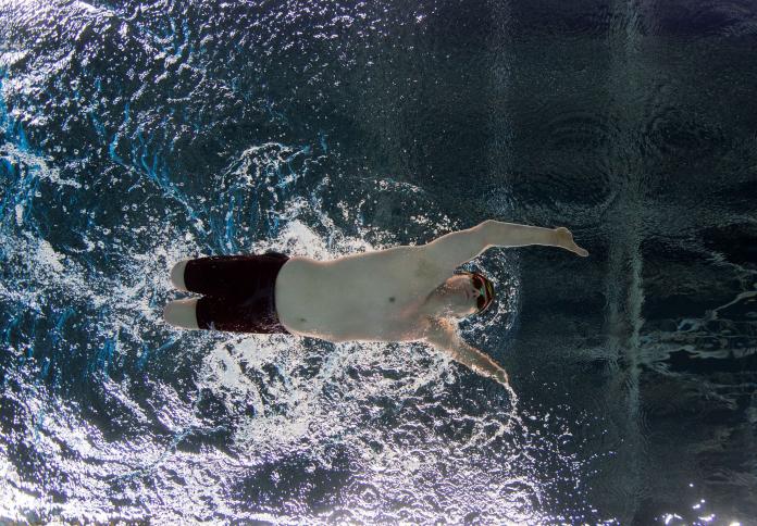 A male swimmer with competes. The photo is taken from below the swimmer.