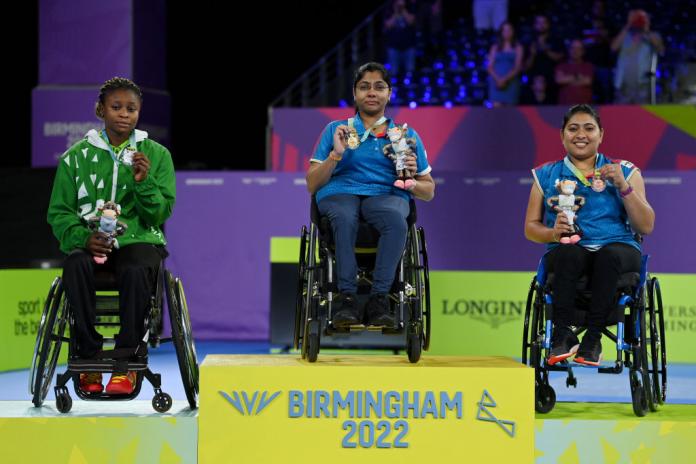 Three female athletes in wheelchairs show their medals while on the podium at the Birmingham 2022 Commonwealth Games.