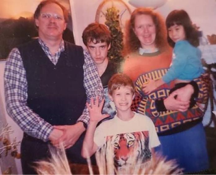 A vintage family photo of a father and mother, two boys and a girl, who is held in the mother's arms.