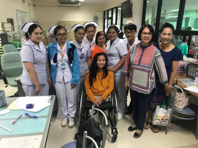 A young woman in a wheelchair poses for a photo surrounded by nurses in hospital scrubs.