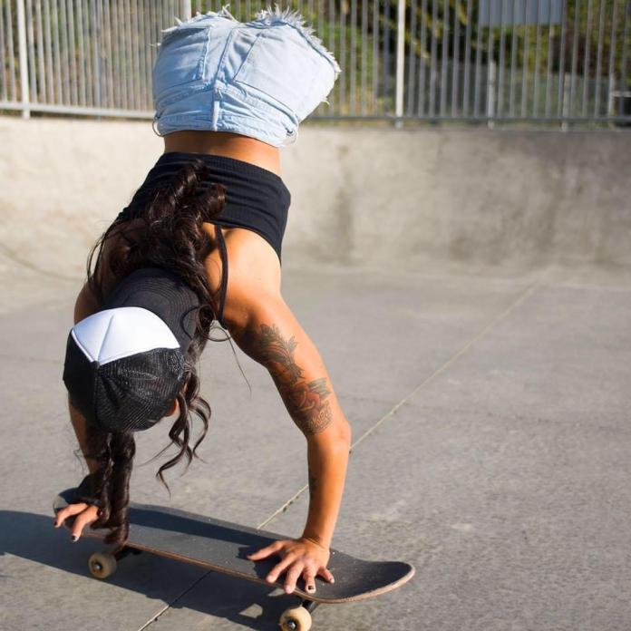 A young female athlete without legs balances upside down on a skateboard.