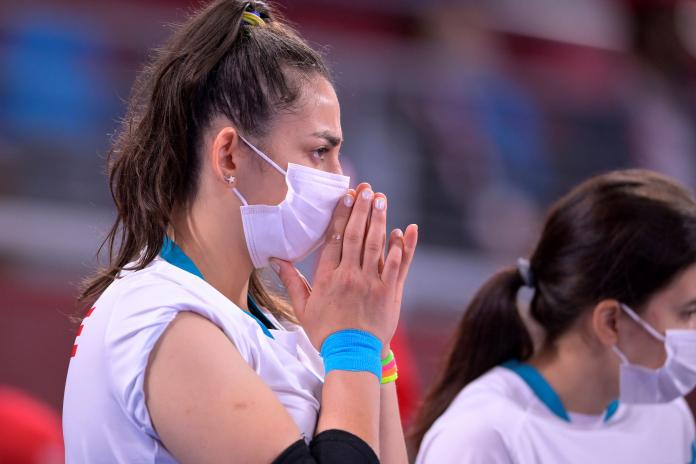 A female goalball player raises her hands to her mouth in a prayer gesture as she watches a game.