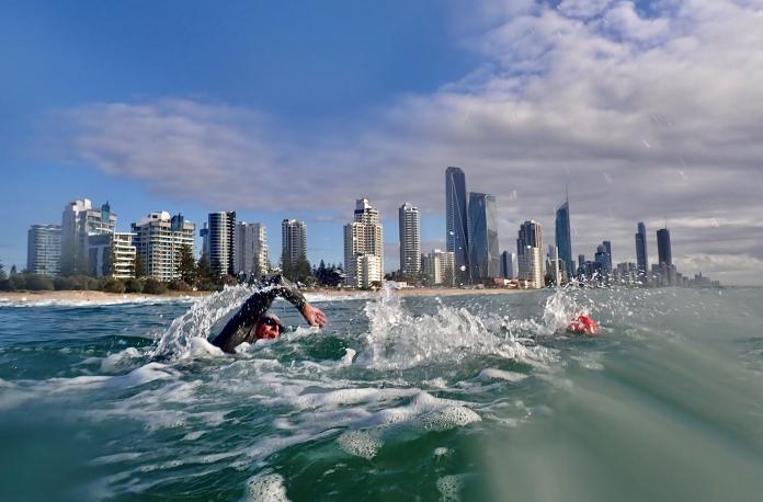 A male athlete takes part in open water swimming, swims in front of tall buildings