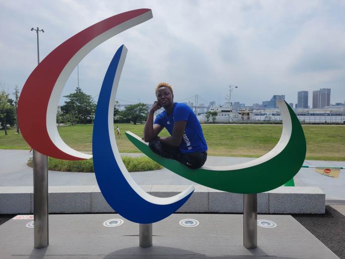 A female athlete wearing a blue T-shirt sits on the Three Agitos monument in Tokyo.