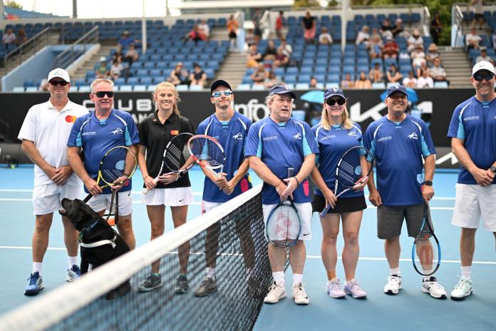 Eight athletes holding tennis racquets stand in a line in front of a net