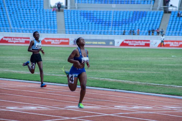 Two female runners near the finish line in a sprint race, as the leader tips her head up with a look of fatigue.