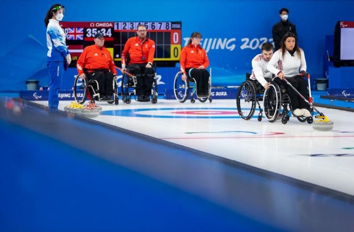 A female wheelchair curler delivers a stone with a stick