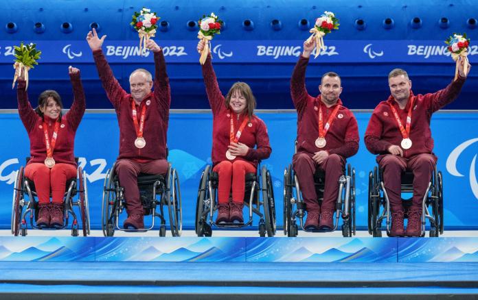 Five athletes on wheelchairs on the podium at the Beijing 2022 Paralympic Games, with bronze medals around their necks.