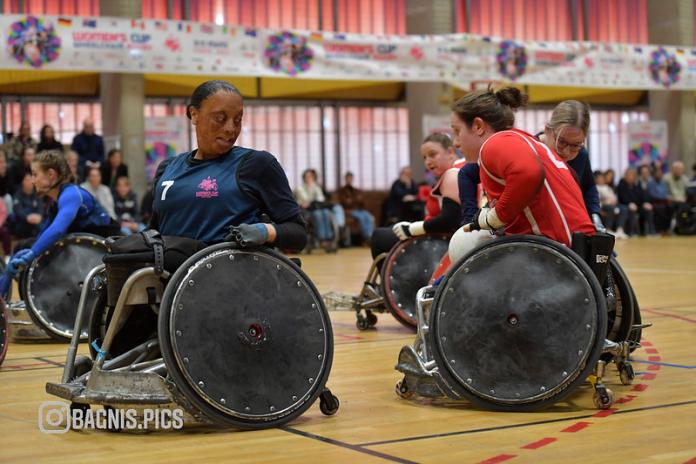 A female wheelchair rugby player in a blue jersey looks plays on court