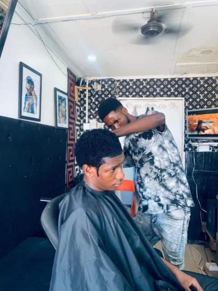 A young man gets his hair cut by another young man at a barbershop.