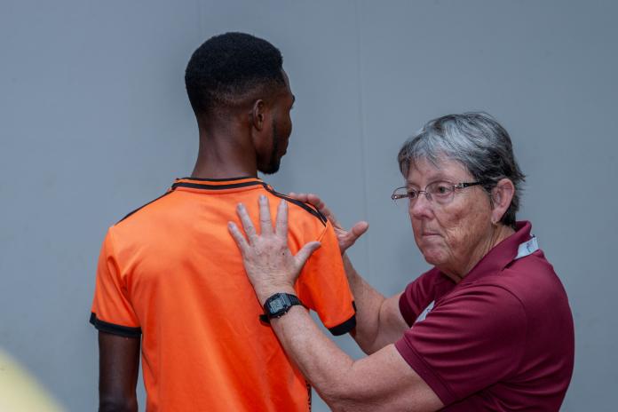 A female coach demonstrates the muscles at work in the shoulder using a male athlete as a model.