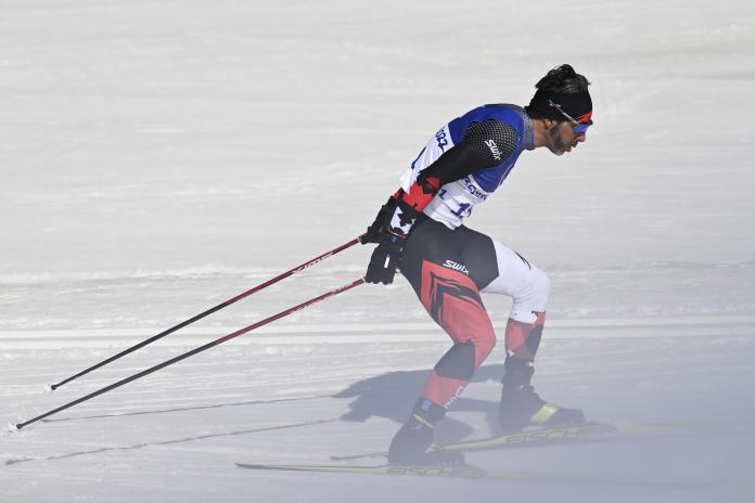 A side view of a male cross-country skier going though a haze of snow during a race.