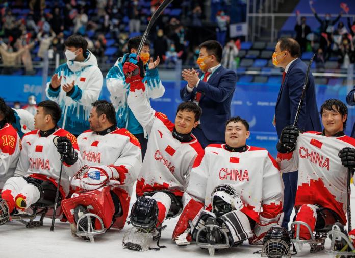 Five male athletes wearing China's red and white jersey celebrate on the rink, while four officials stand behind them clapping their hands