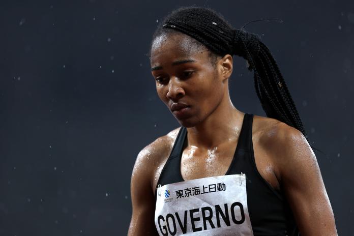 A close up of a female sprinter as she looks down after a race while rain falls around her.