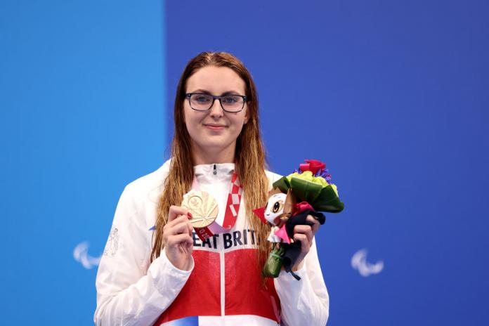 A female Para athlete holds the gold medal and a flower bouquet
