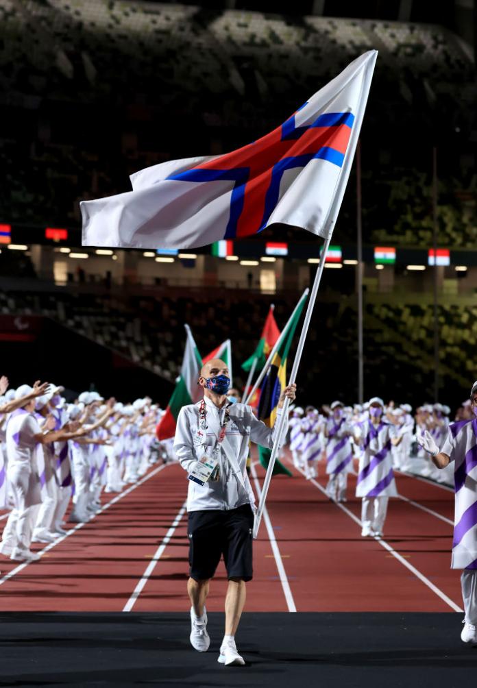 A male athlete with a right hand amputation carries the flag of the Faroe Islands during the Tokyo 2020 Closing Ceremony.