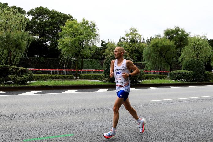 A male athlete with a right arm amputation below the elbow runs alone on an asphalted road.