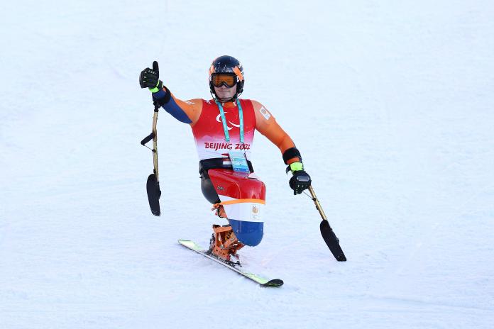A male sit skier gives a thumbs up on the finish line of a Para alpine skiing course after learning that he won the silver medal.