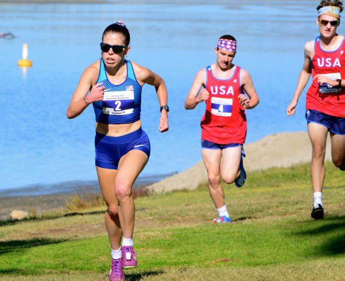 A female athlete runs ahead of two male athletes.