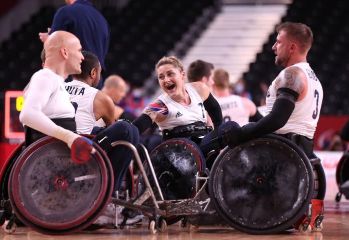 A female wheelchair rugby player speaks with two male wheelchair rugby athletes on the court.