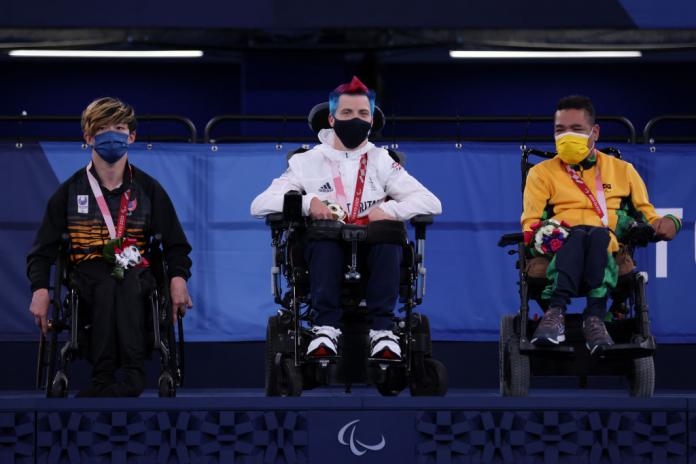 Three male athletes on wheelchairs are on the podium.