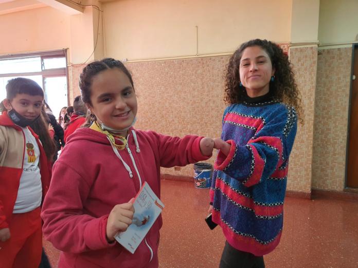 A young girl and a Para athlete, both missing their left hands, bump their arms together at a school.