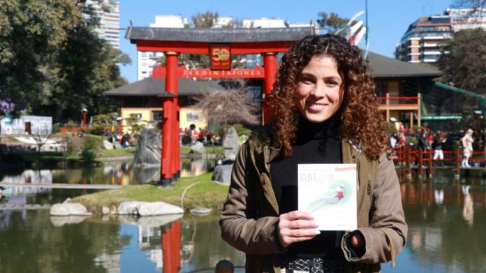 A female athlete without a left hand holds up a book at a Japanese garden in Argentina.