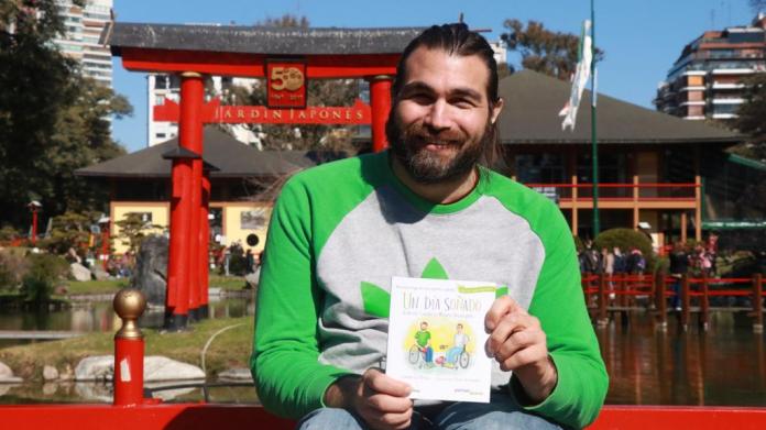 A man in a green sweatshirt holds up a book at a Japanese garden in Argentina.