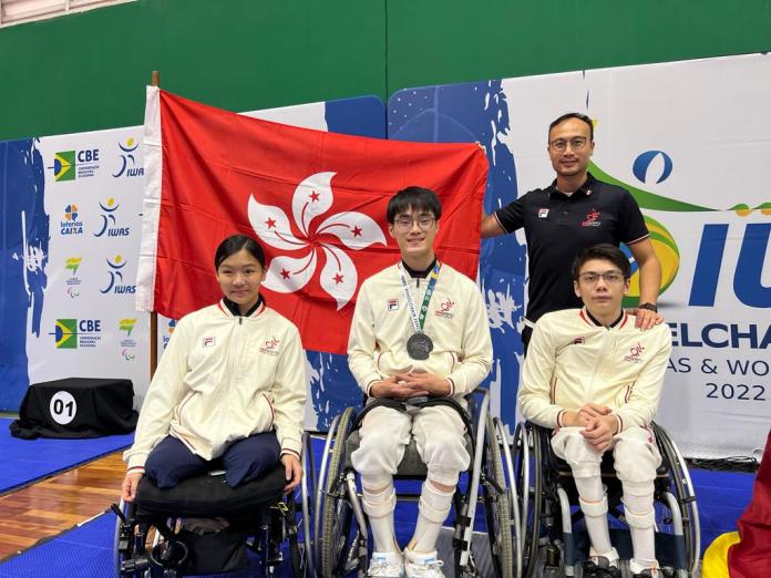 Three young wheelchair fencers pose for a photo together with the coach and the Hong Kong flag.