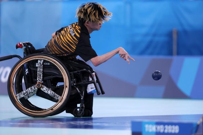 A photograph of a male boccia athlete taken from the side.