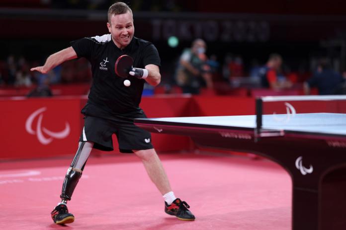 A male athlete plays Para table tennis. He uses a prosthetic leg.