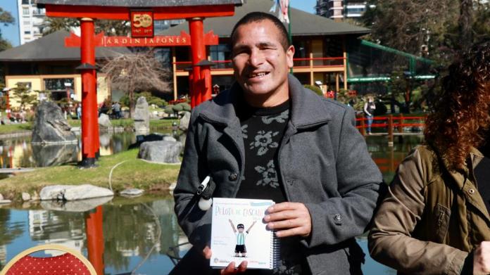 A man with a vision impairment holds up a book as he poses in a Japanese garden in Argentina.