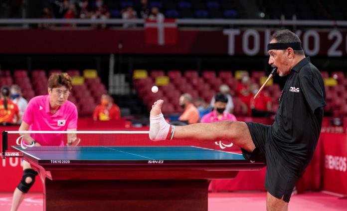 A male Para table tennis athlete serves the ball using his right foot