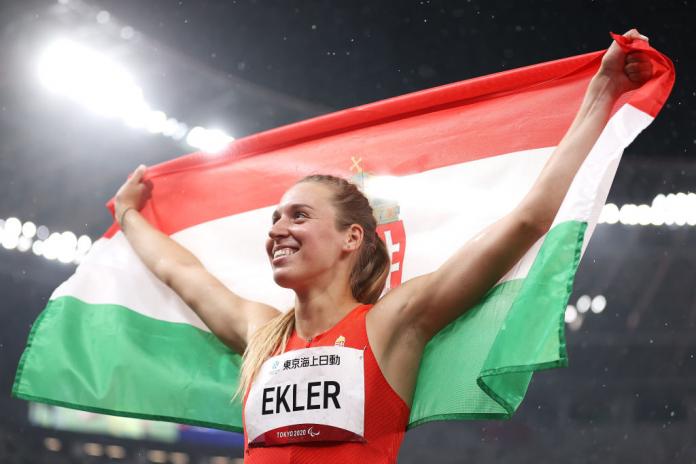 A female athlete spreads her arms while holding the flag of Hungary.