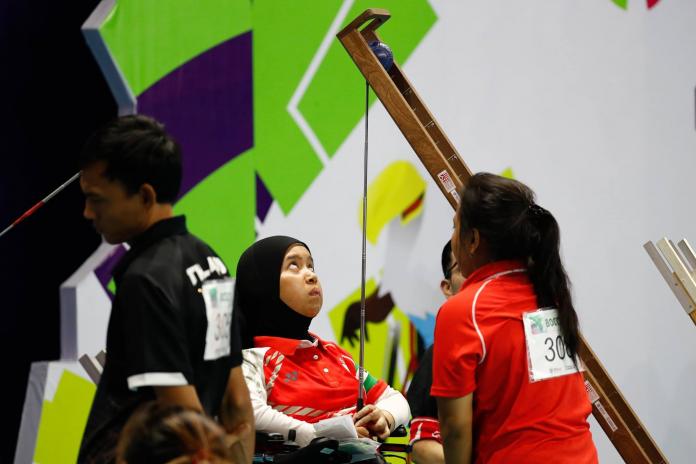 A female athlete looks up at her wooden ramp. A female assistant stands in front of her, next to the ramp.