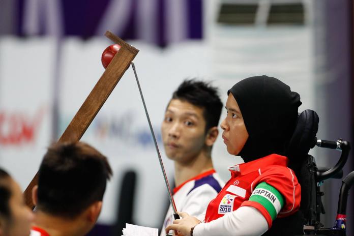 A photo taken from the side of a boccia athlete preparing to deliver a red ball on a ramp.